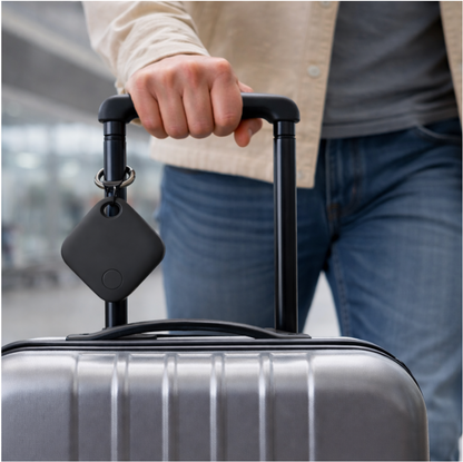 Lifestyle Image with a man holding a suitcase handle with the air tag GPS tracker product (colour back) attached to the suitcase handle, focus on the air tag tracker product in the image, front angle.